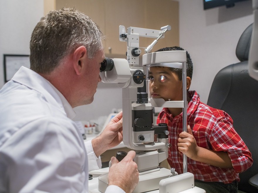 Male optometrist performing eye exam on child