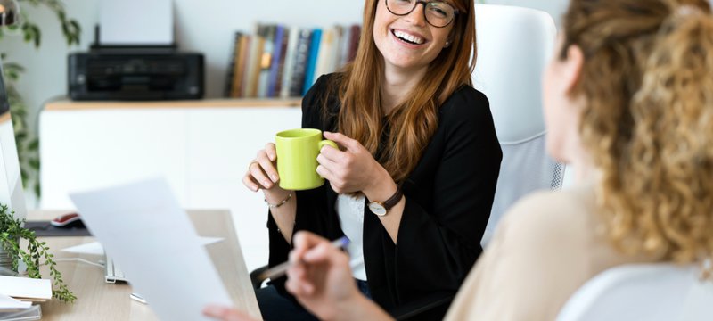Two women in business attire talking and laughing.