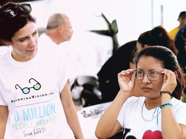 Young woman watching another woman try on new glasses at a vision event.