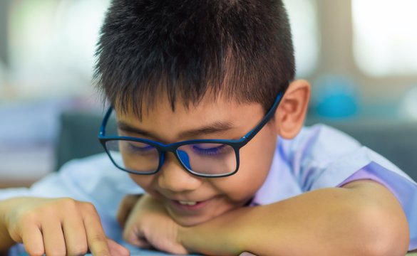 Young boy wearing glasses and reading a book.